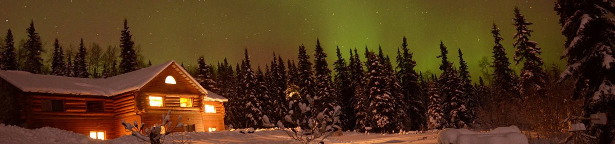 Northern Lights and log cabin in Alaska night sky