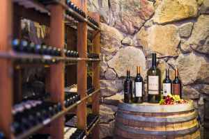 Wine bottles in the wine cellar at Lares de Chacras Boutique Hotel, Chacras de Coria area of Mendoza, Mendoza Province, Argentina. The bottles of wine are on a barrel, there are grapes next to them.