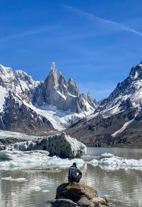 The Best Tour of Argentina 4 A man crouches down in front of a lake, glaciers, and mountains in Los Glaciares National Park. He is wearing winter hiking gear.