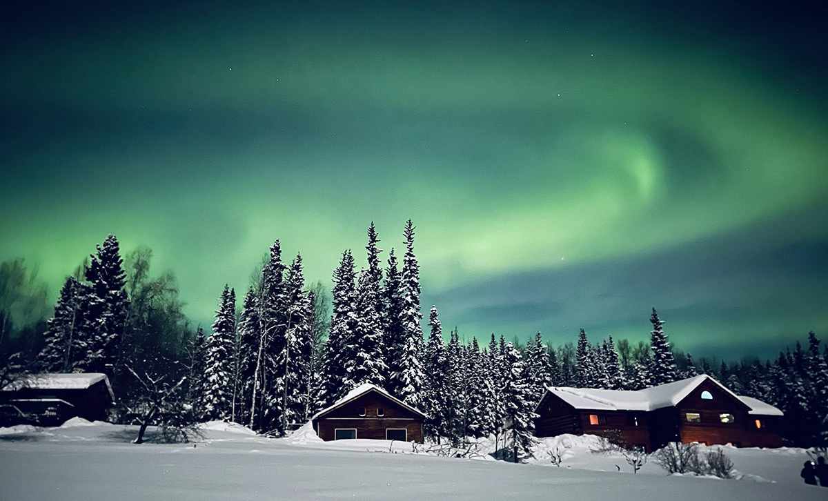 Northern Lights Aurora Borealis in Alaska with snow covered trees and hut 