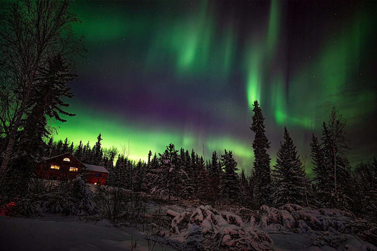 Log cabin with beams of green aurora borealis in Alaska