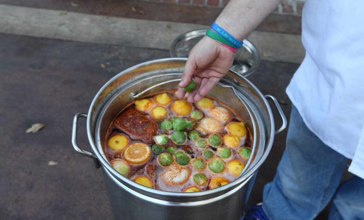 Someone hand next to a a large pot containing a traditional Louisiana seafood boil 