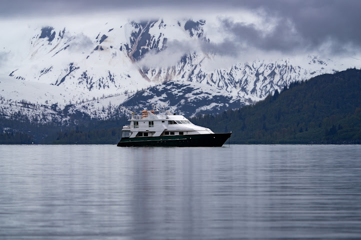 A yacht sails through the Inside Passage of Alaska, flanked by snowy mountains
